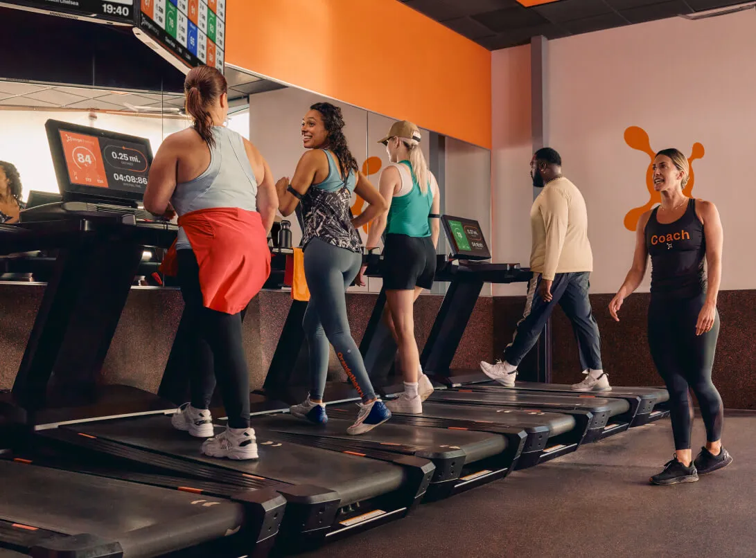 Orangetheory Fitness members walking and running on treadmills while a coach provides guidance in a high-energy Gym.